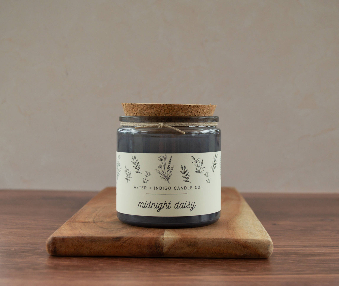 Candle jar labeled 'midnight daisy' on a wooden board with a beige background