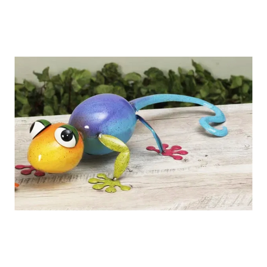 Colorful metal gecko on a wooden surface with a green leafy background