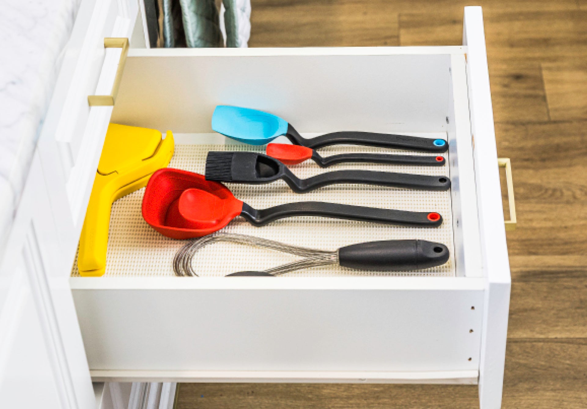 Set of colorful kitchen utensils in a white drawer on a wooden floor.