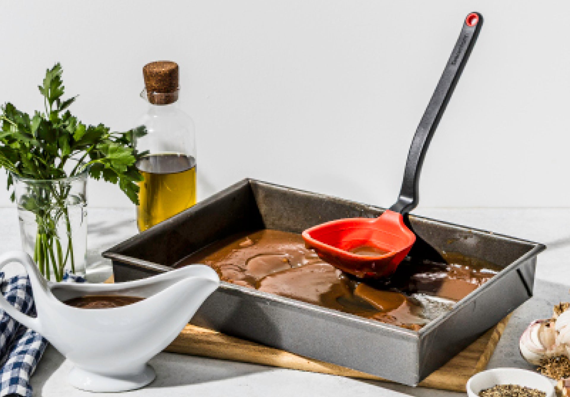 Roasting pan with beef, red ladle, and oil bottle on a white surface