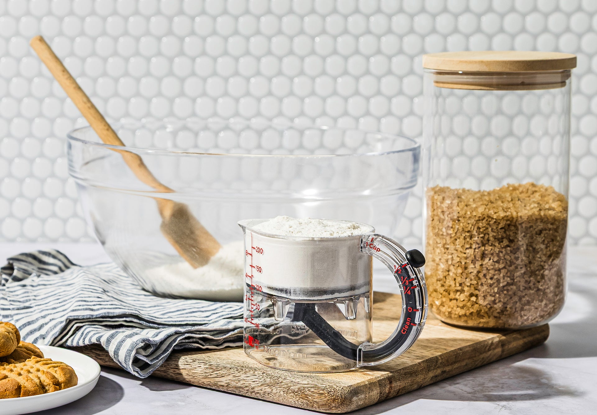 Baking setup with glass bowl, measuring cup, and jar on a wooden board.