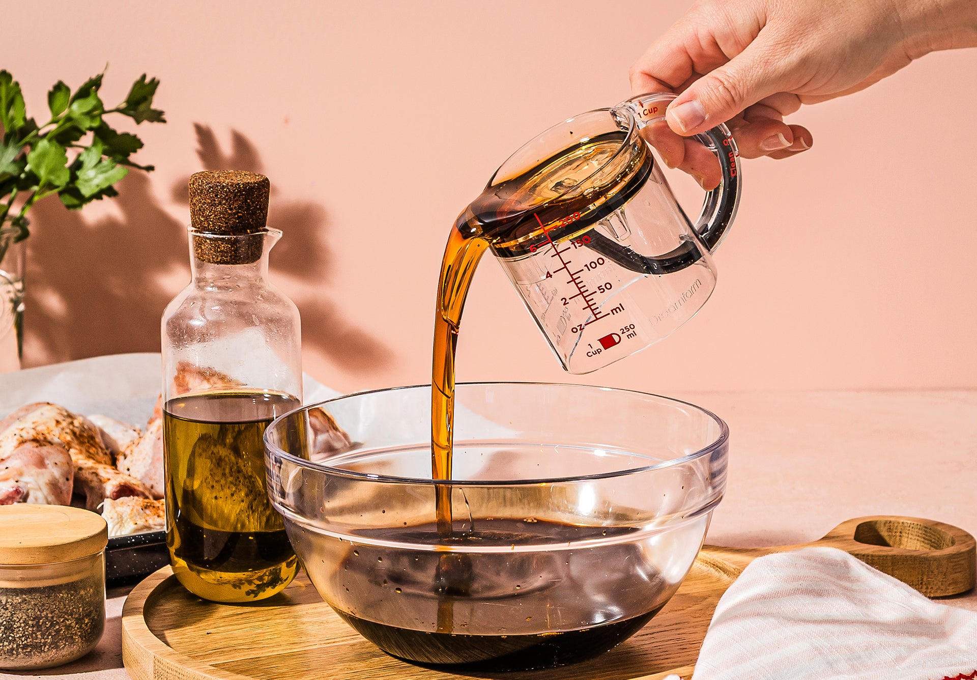 Hand pouring liquid from a measuring cup into a glass bowl on a wooden surface.