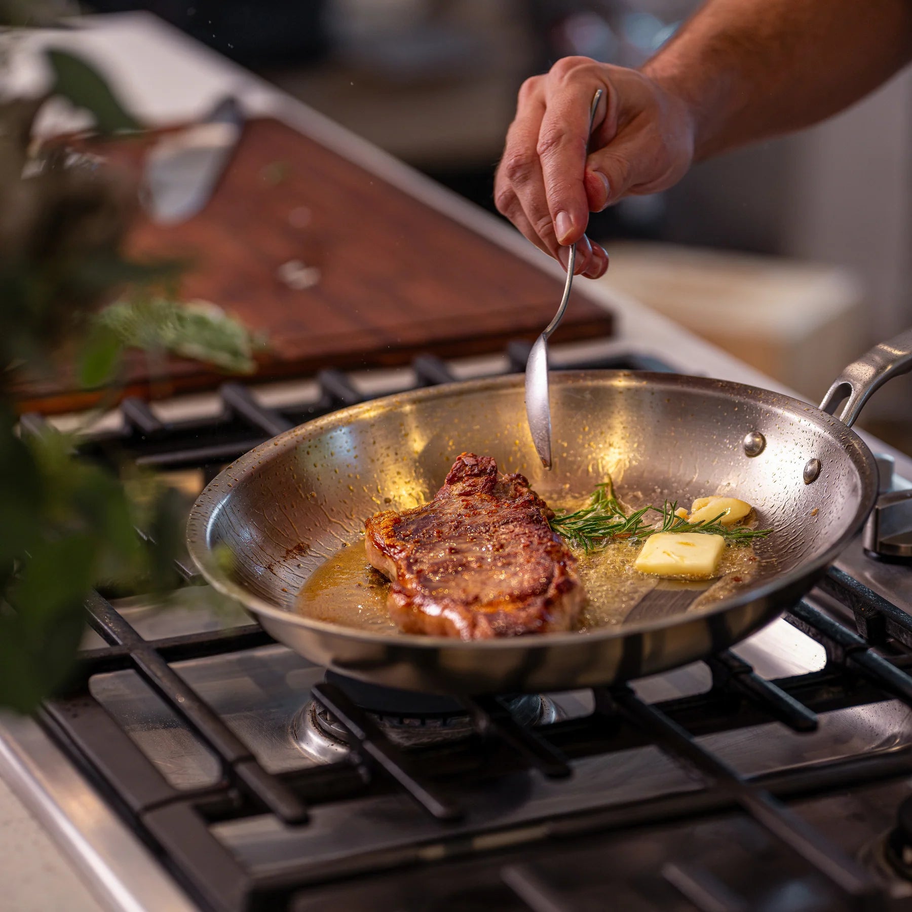 Person cooking steak in a pan on a stove with butter and herbs.