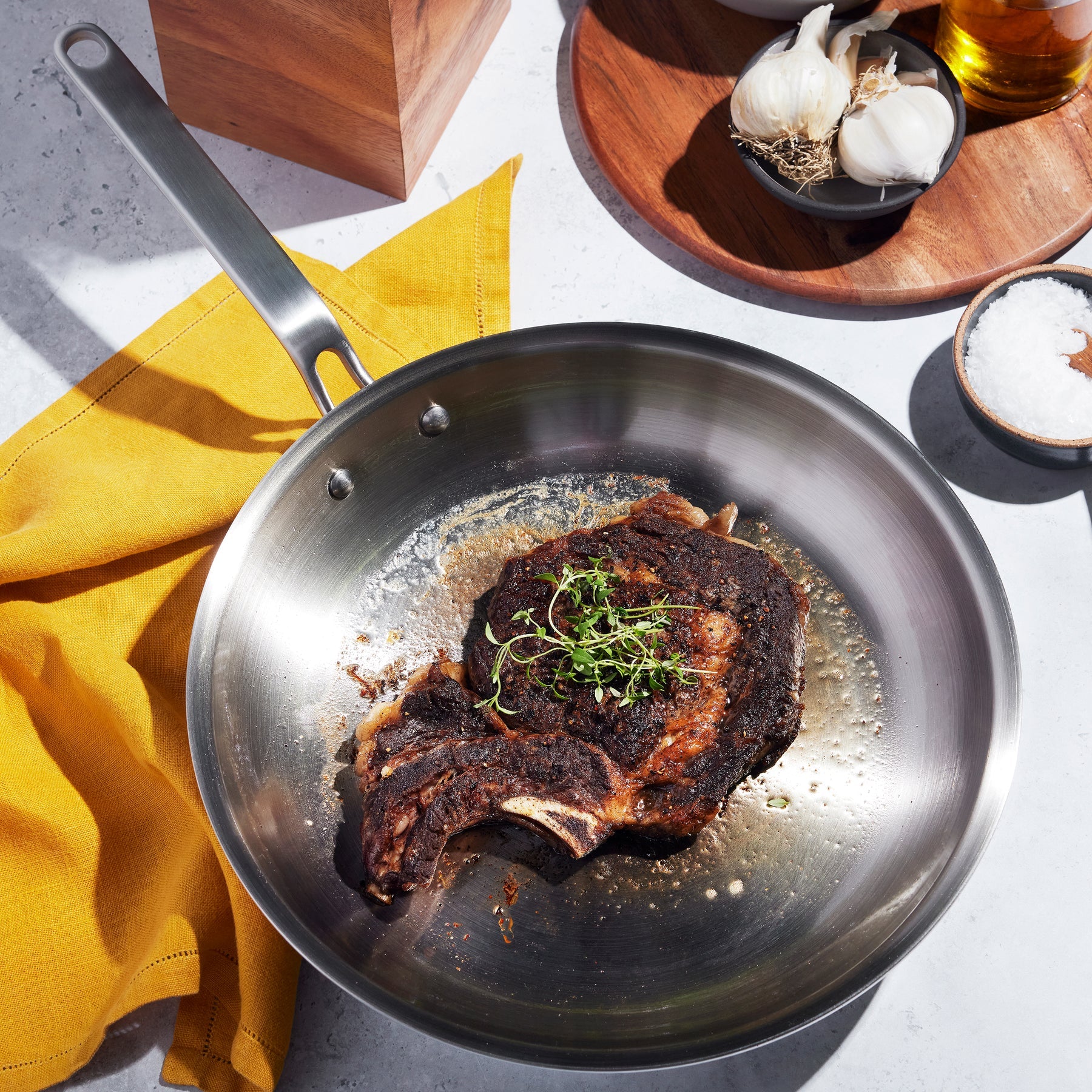Seared steak in a frying pan on a table with a yellow napkin and various seasonings.