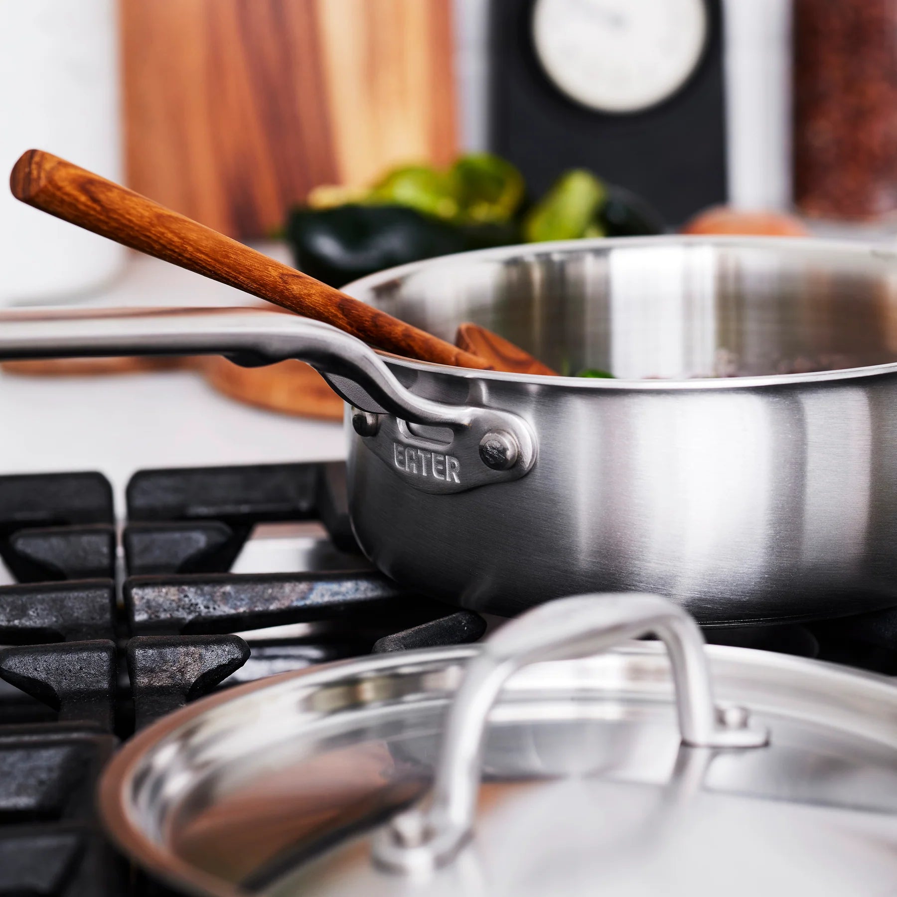 Stainless steel cookware set on a stove with a wooden spoon.