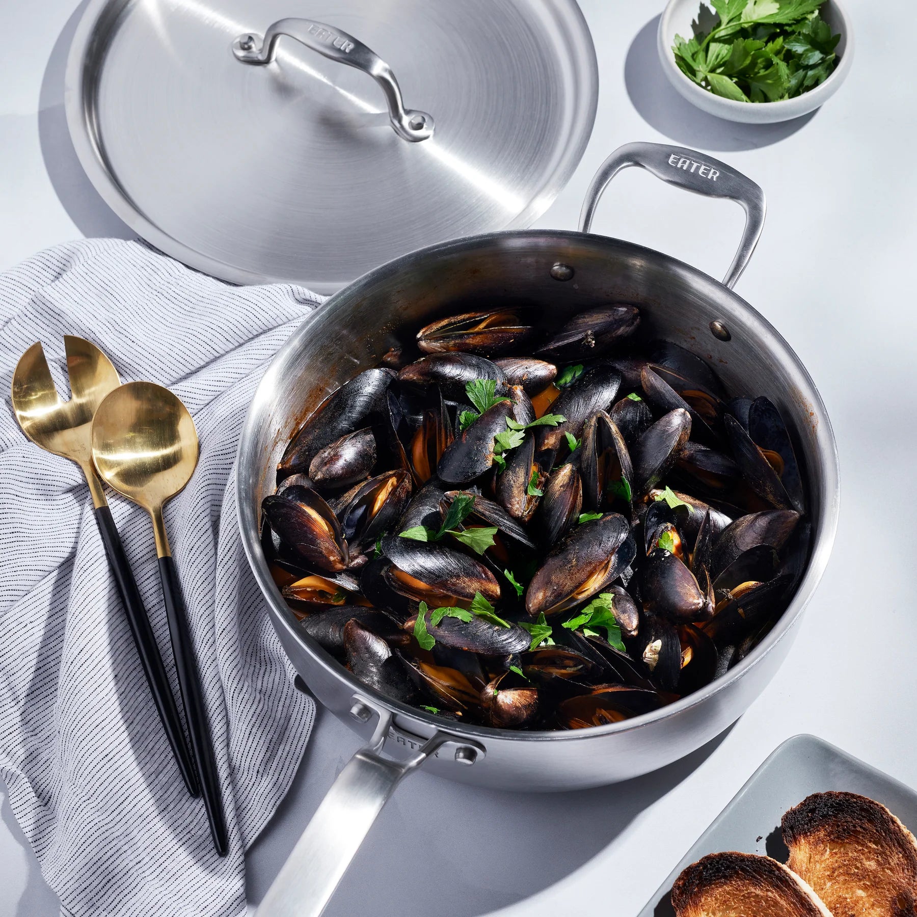 Stainless steel pot with mussels and herbs on a light background