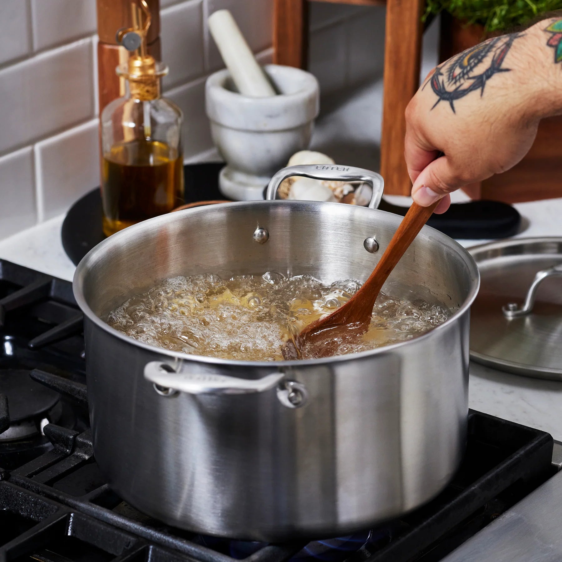 Person stirring boiling pasta in a pot with a wooden spoon on a stove.
