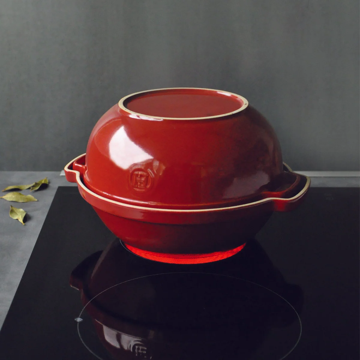 Red ceramic pot with lid on a black surface against a gray background