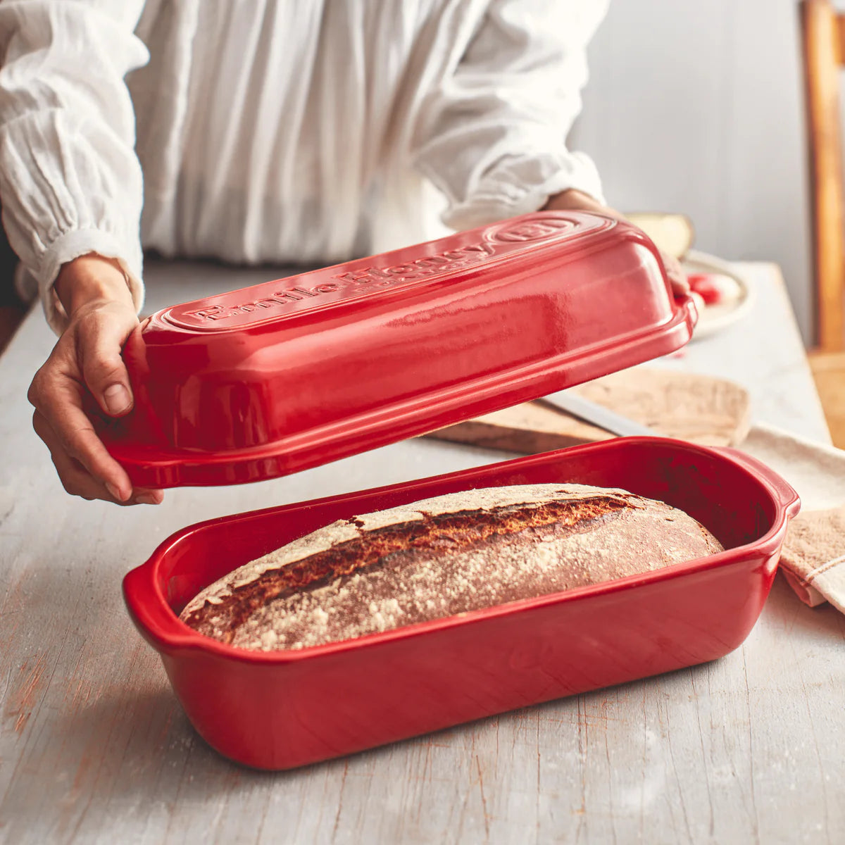 Red bread loaf pan with a baked loaf of bread inside, held by a person.