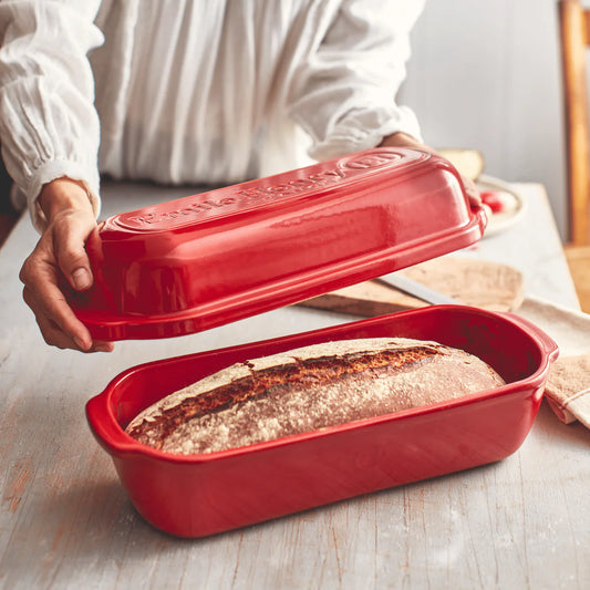 Red bread loaf pan with a baked loaf of bread inside, held by a person.