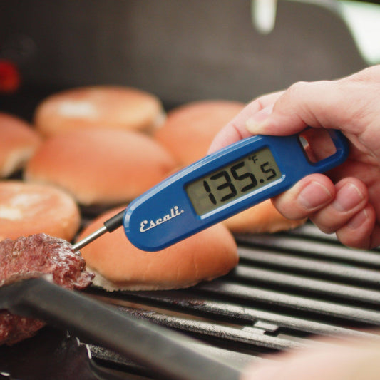 Hand holding a blue digital thermometer over a burger on a grill