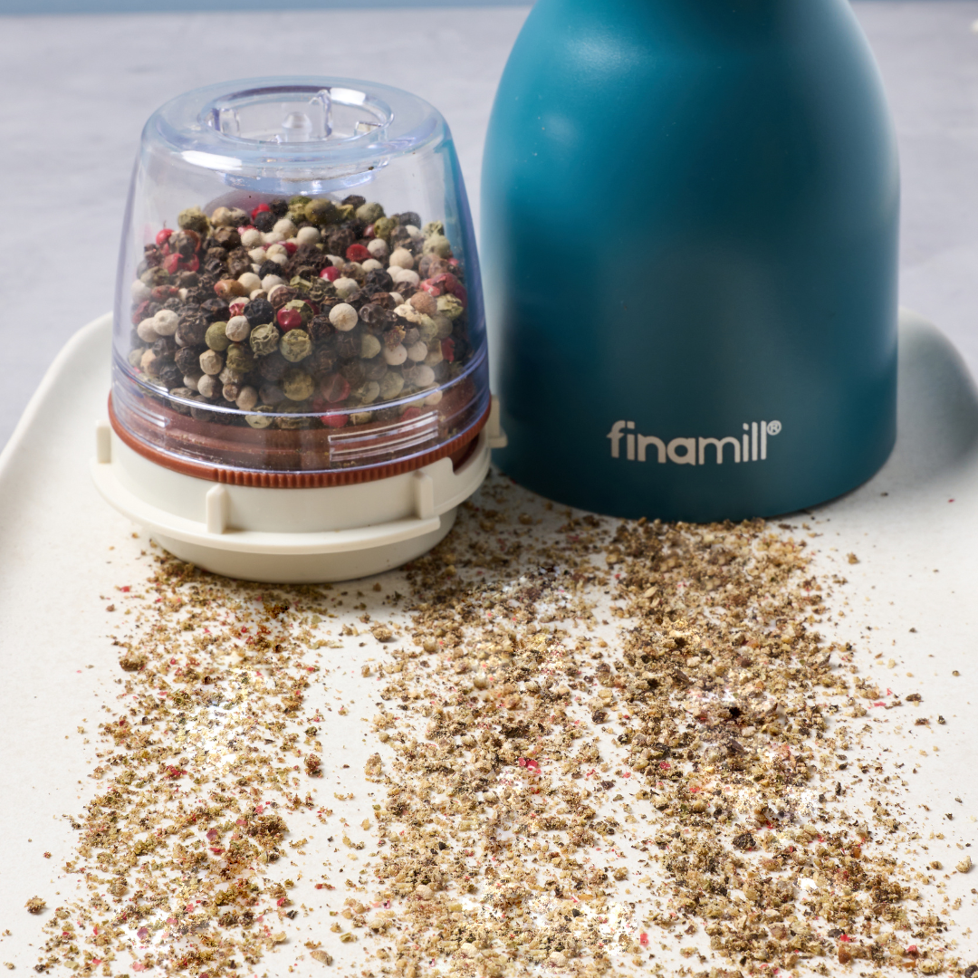 Pepper grinder with ground pepper on a white surface, featuring the brand 'finamill'.