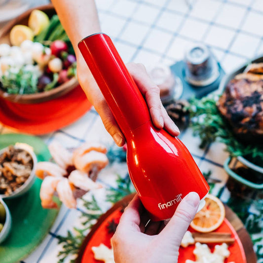 Red kitchen tool held by a person with a festive table setting in the background