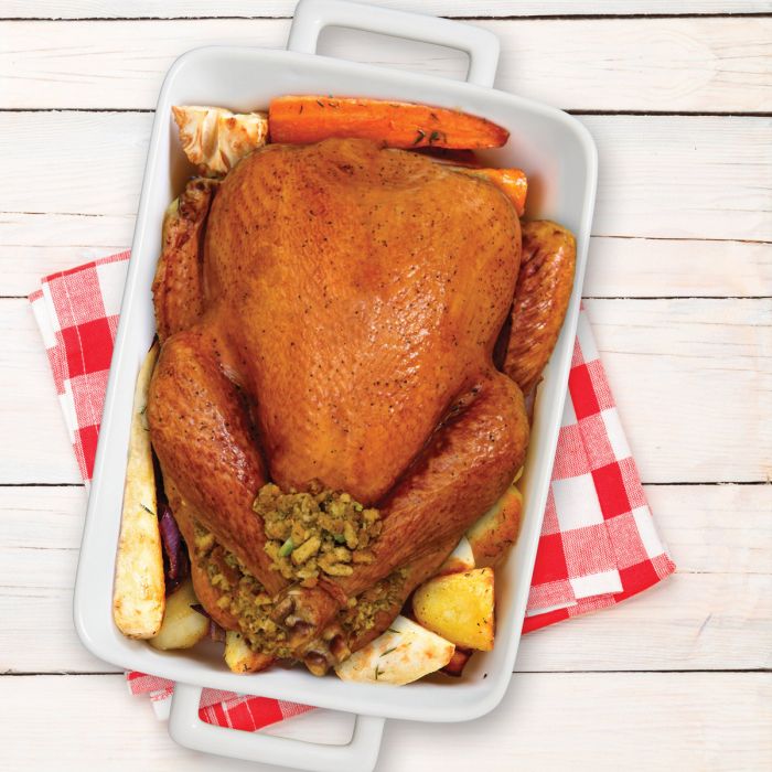 Roasted turkey with stuffing in a white baking dish on a wooden surface.