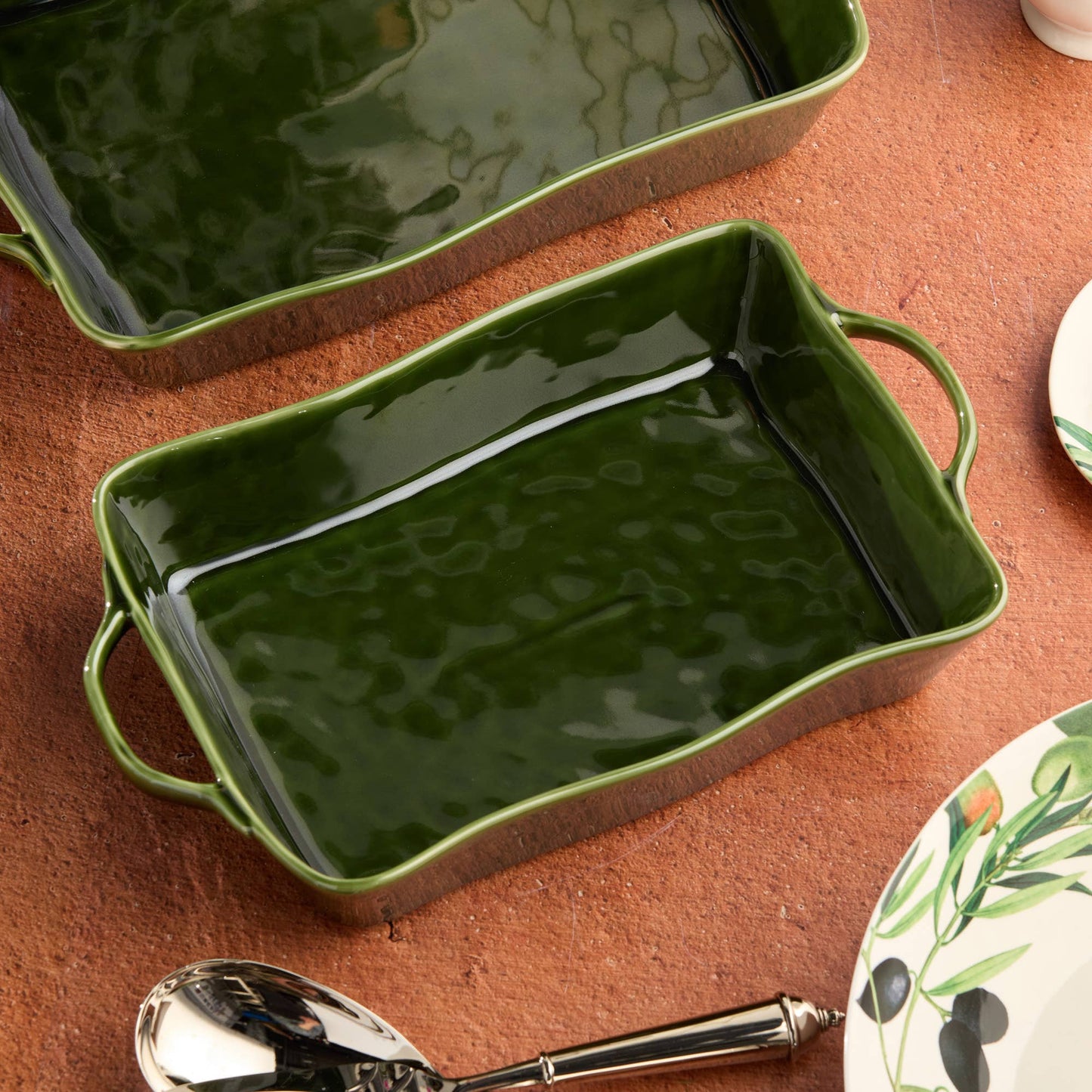 Green rectangular ceramic baking dish on a brown surface with a spoon and floral plate.
