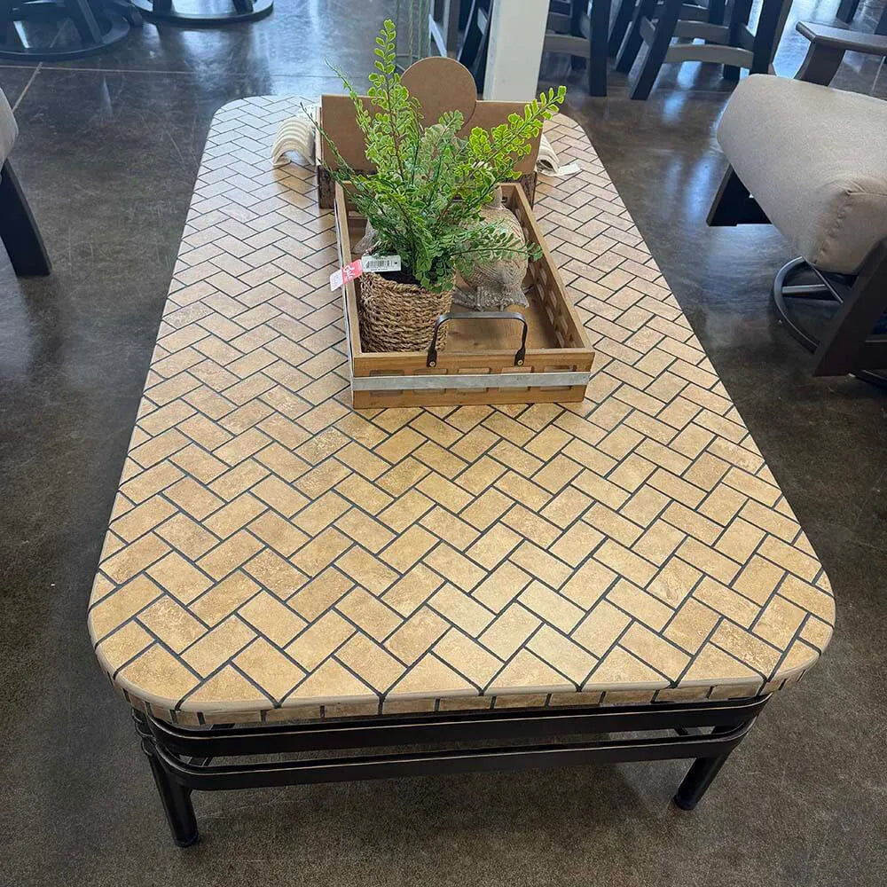 Patio Coffee table with a herringbone pattern top and a plant in a woven basket on top.