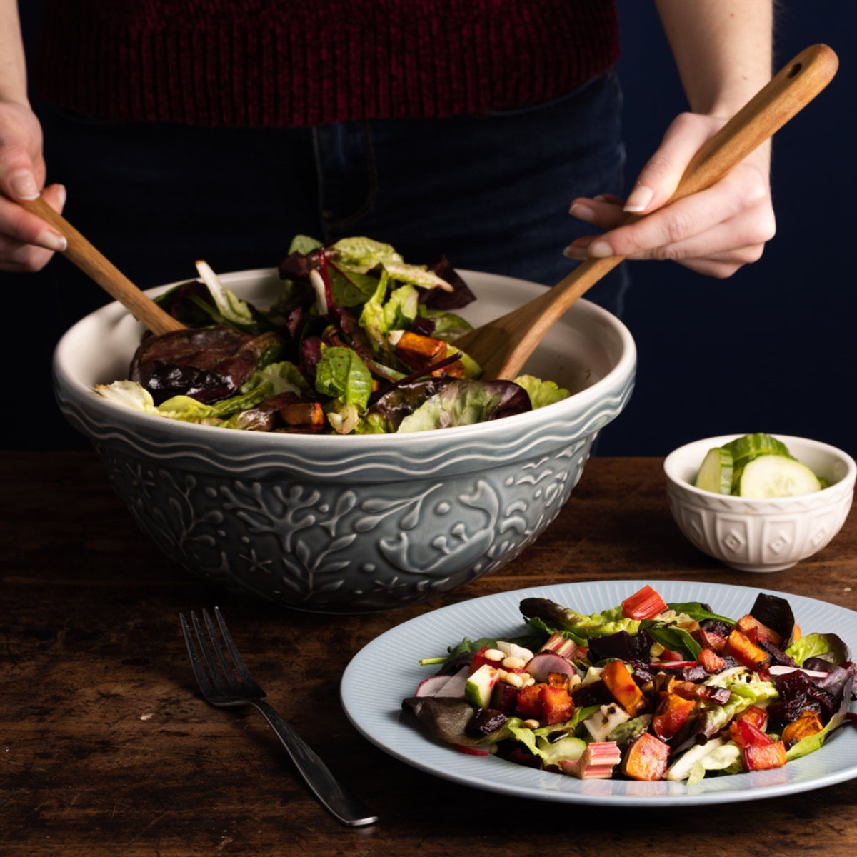 Person serving salad from a Mason Cash Crab bowl onto a plate on a wooden table.