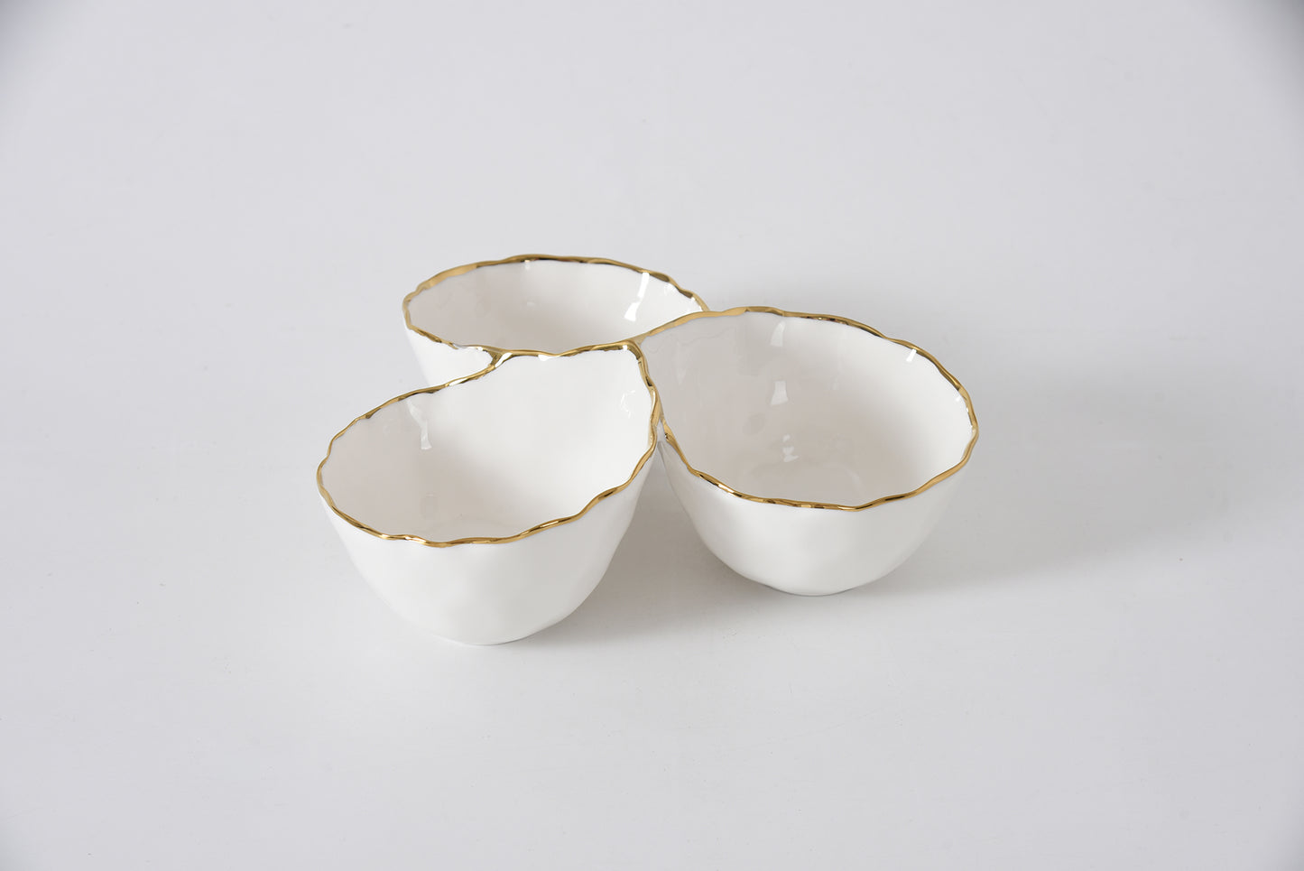 Three white ceramic bowls with gold rims on a light gray background