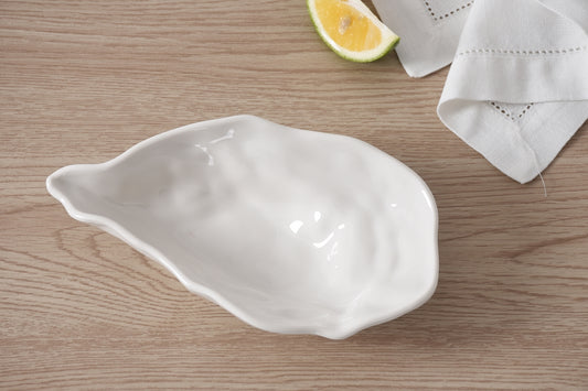 White melamine shell-shaped dish on a wooden surface with a lemon wedge and white napkin.