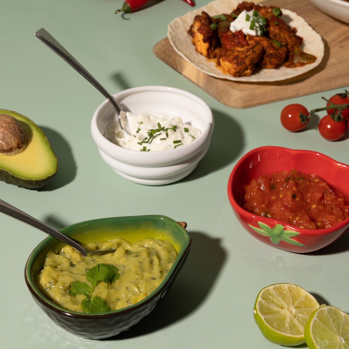 Assorted Mexican food items including guacamole, salsa, sour cream, and a plate of chicken tacos on a green surface.