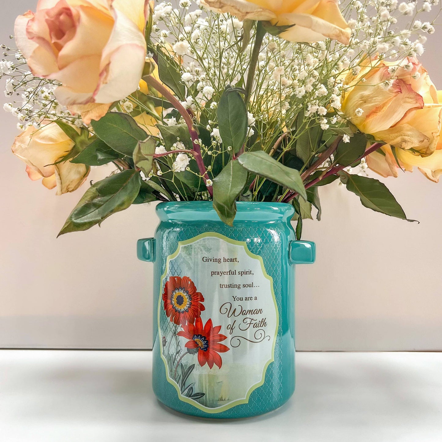 Turquoise jar vase with flowers and a decorative label on a white background