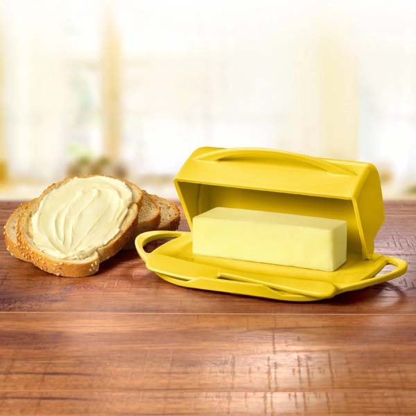 Yellow butter dish with a stick of butter on a wooden surface next to a slice of bread.