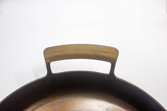 Close-up of a carbon steel skillet handle and rim against a plain white background.