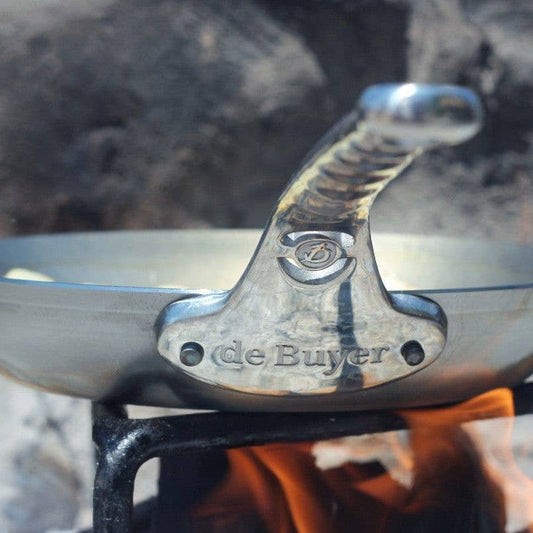 Close-up of a carbon steel frying pan handle with 'de Buyer' branding against a blurred natural background