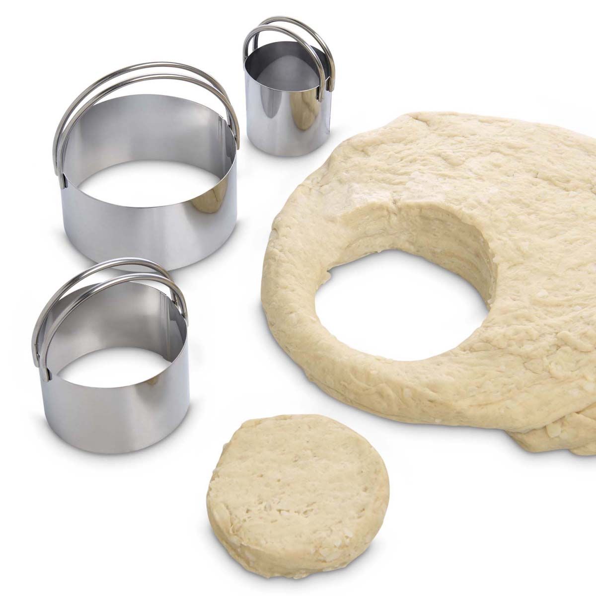 Three stainless steel biscuit cutters next to a ball of biscuit dough on a white background