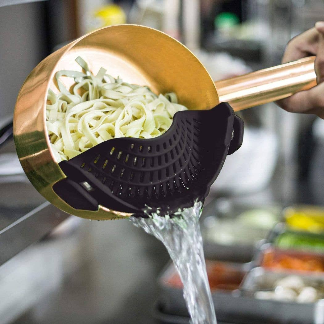 Copper-colored pan with a black silicone scoop pouring water over noodles in a kitchen setting.