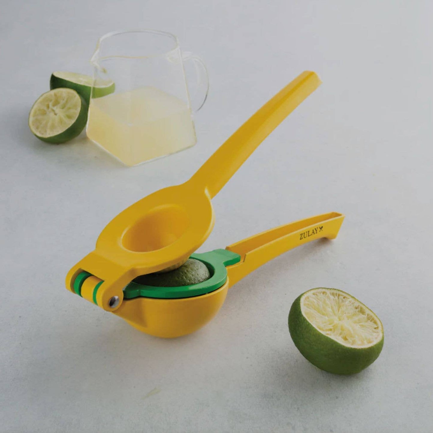 Yellow lemon squeezer with a glass of lime juice and half a lime on a light gray background