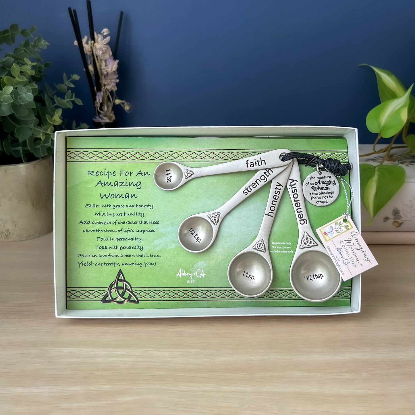 Set of silver measuring spoons with engraved words on a green card with text, placed on a wooden surface.