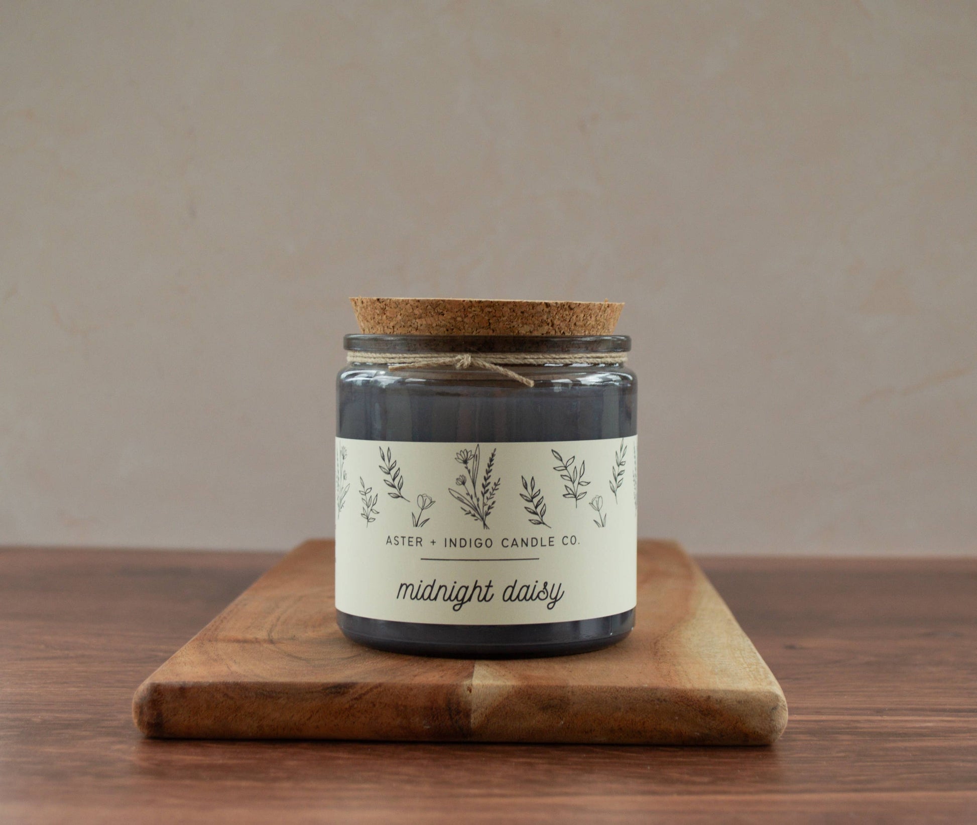 Candle jar labeled 'midnight daisy' on a wooden board with a beige background