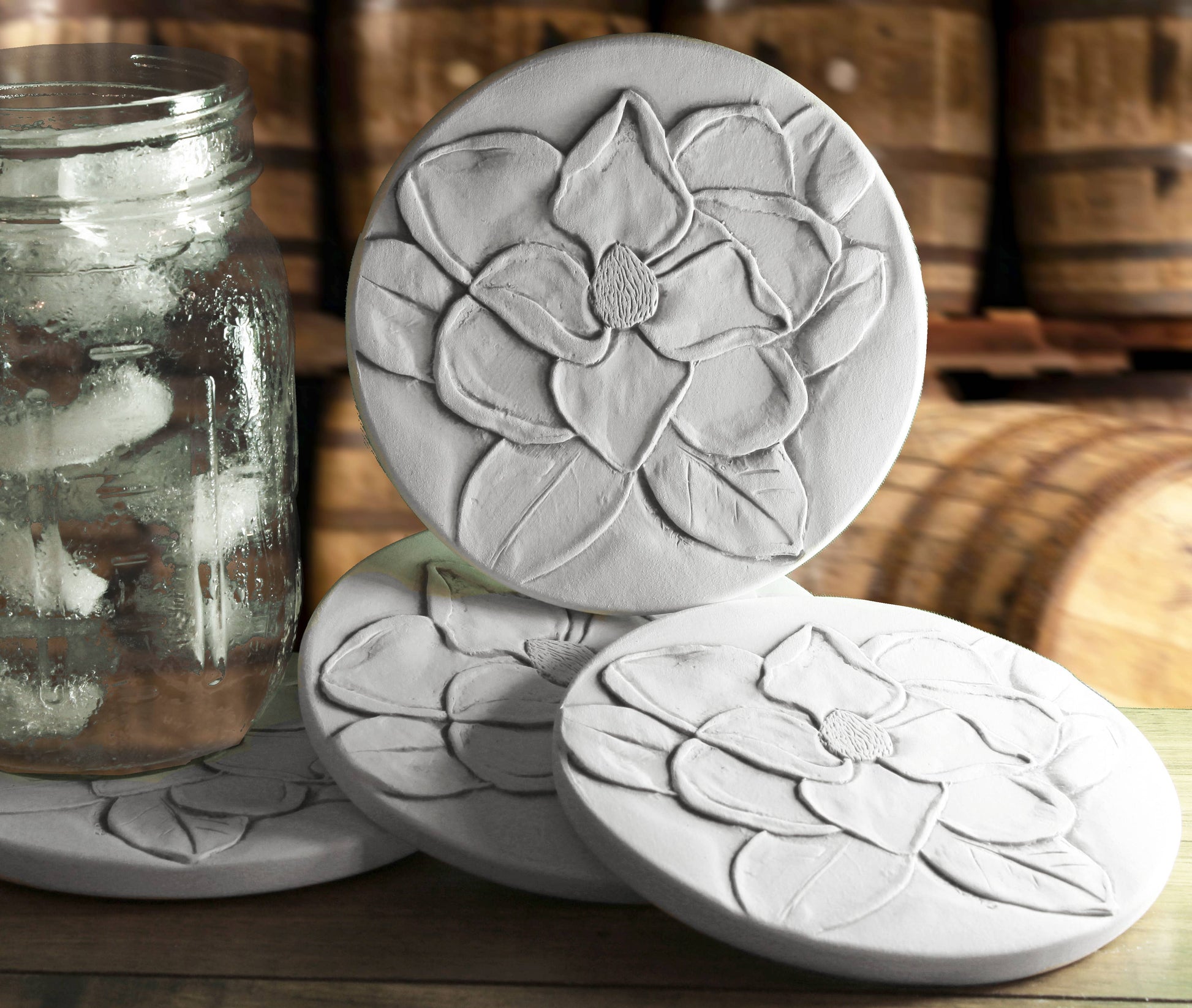 Four ceramic coasters with floral designs on a wooden surface.