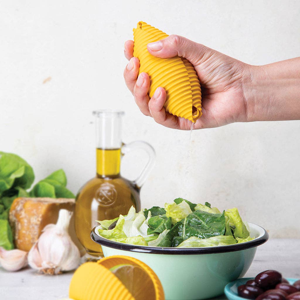 Hand squeezing a yellow lemon squeezer over a salad with olive oil and garlic in the background.