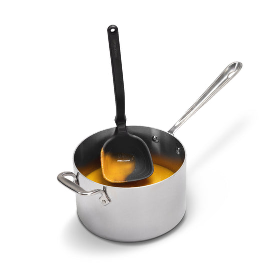 Stainless steel saucepan with a black ladle on a white background