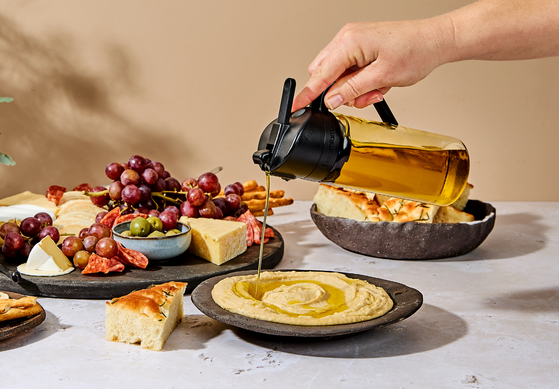 Oileroo being used to pour oil on a plate of humus with bread
