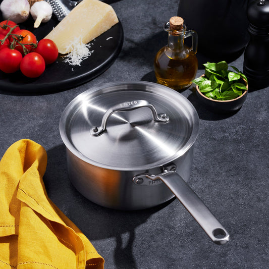 Stainless steel pot with lid on a dark surface with kitchen ingredients.