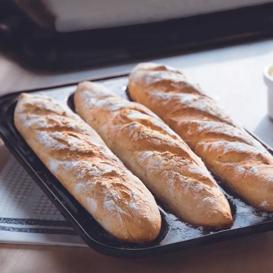 Three freshly baked baguettes on a baking tray with flour.
