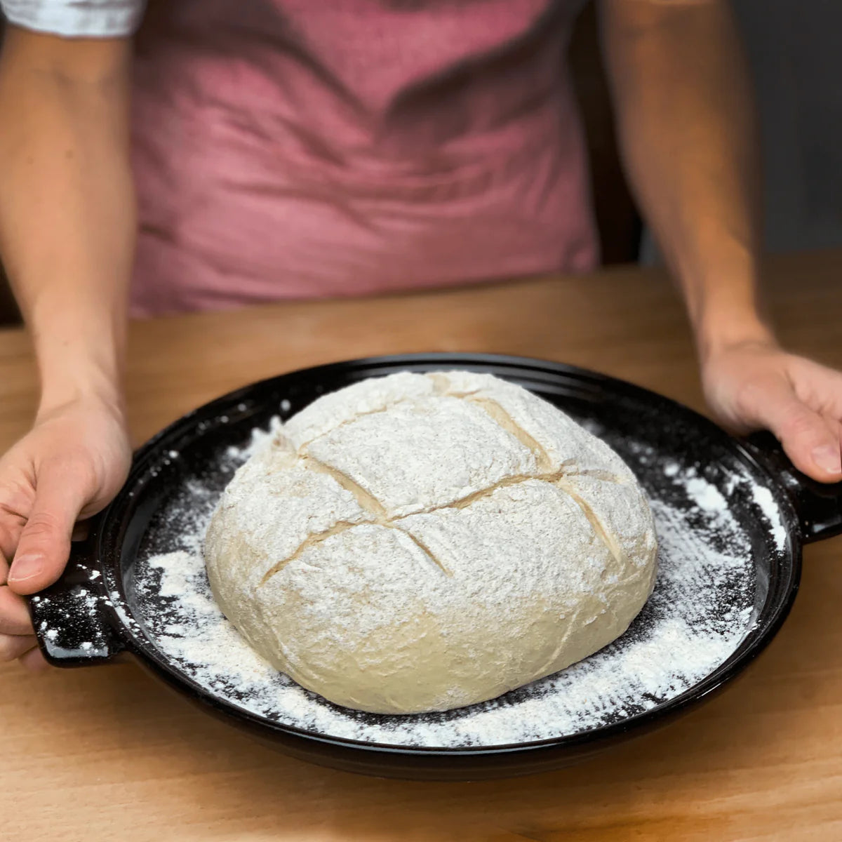 Baked bread on a black tray with flour, held by a person in a kitchen setting.