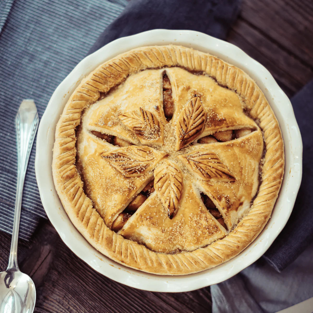 Apple pie with decorative crust in a white dish on a wooden table.