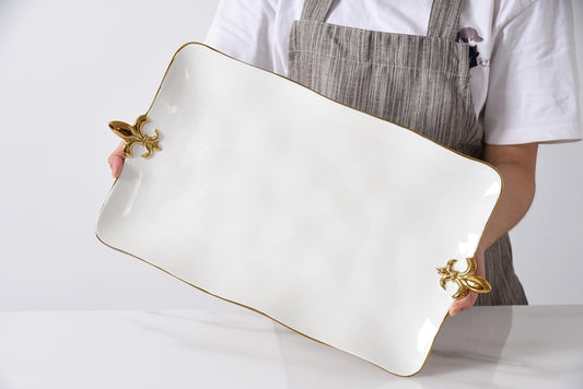 Person holding a white platter with fleur de lis gold accent handles