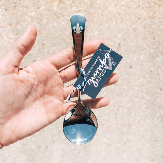 Hand holding a silver spoon with a blue accent and a 'Gumbo Spoon' tag.