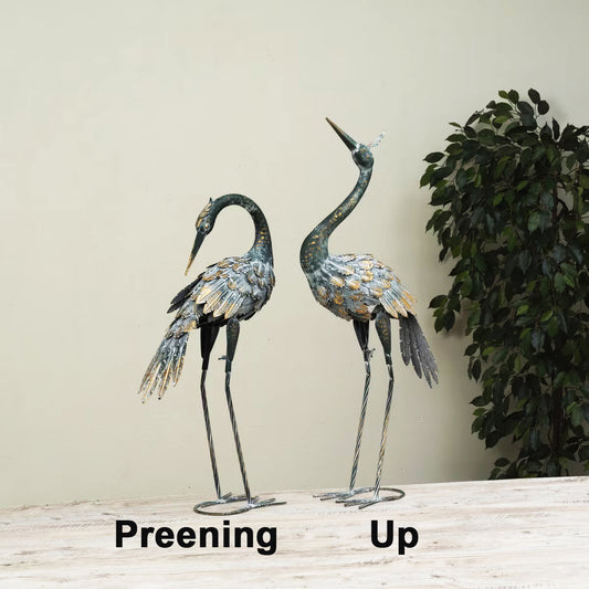 Two decorative cranes on a wooden surface with a plant in the background.