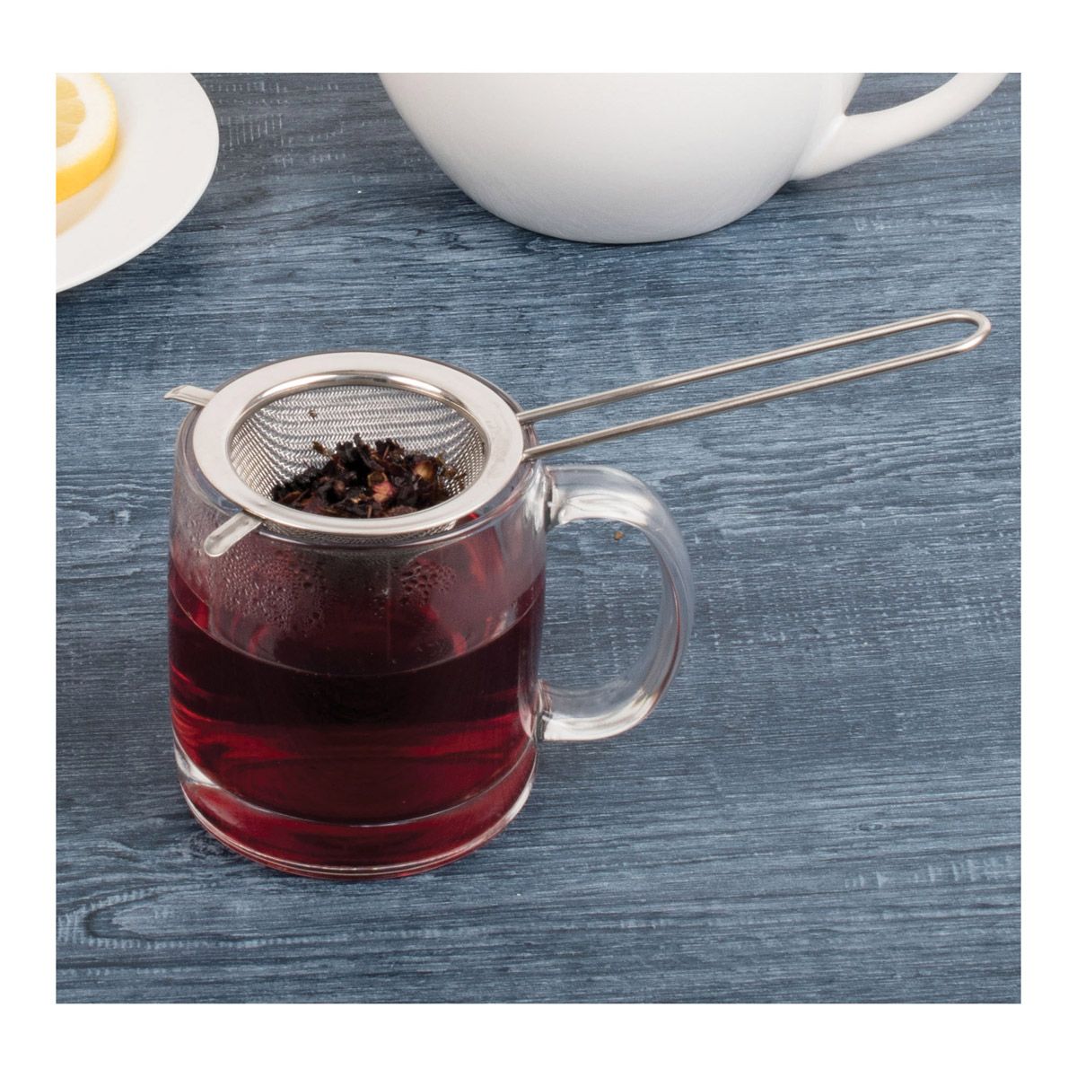 Clear mug with metal tea infuser filled with red liquid on a blue wooden surface.