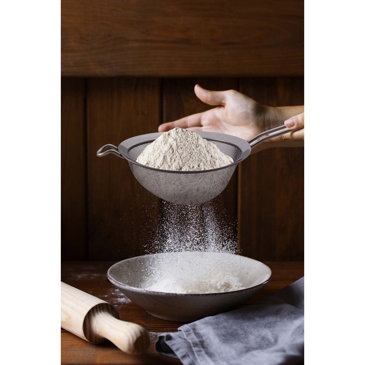 Person sifting flour into a bowl on a wooden surface