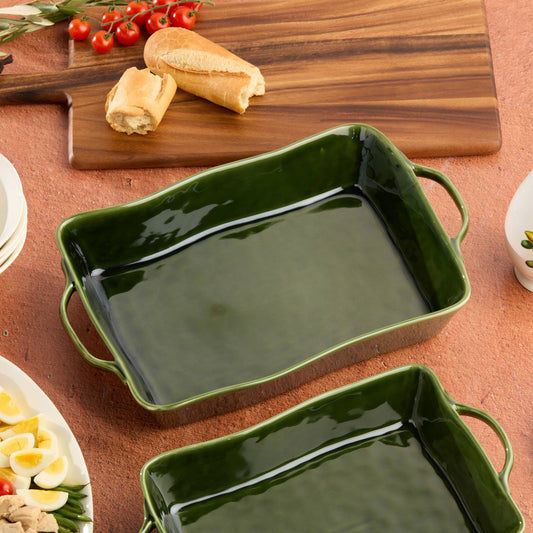Green ceramic baking dish on a wooden table with bread and tomatoes.