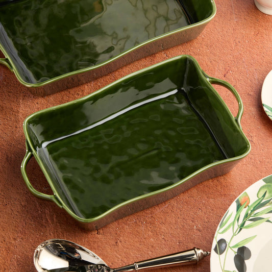 Green rectangular ceramic baking dish on a brown surface with a spoon and floral plate.