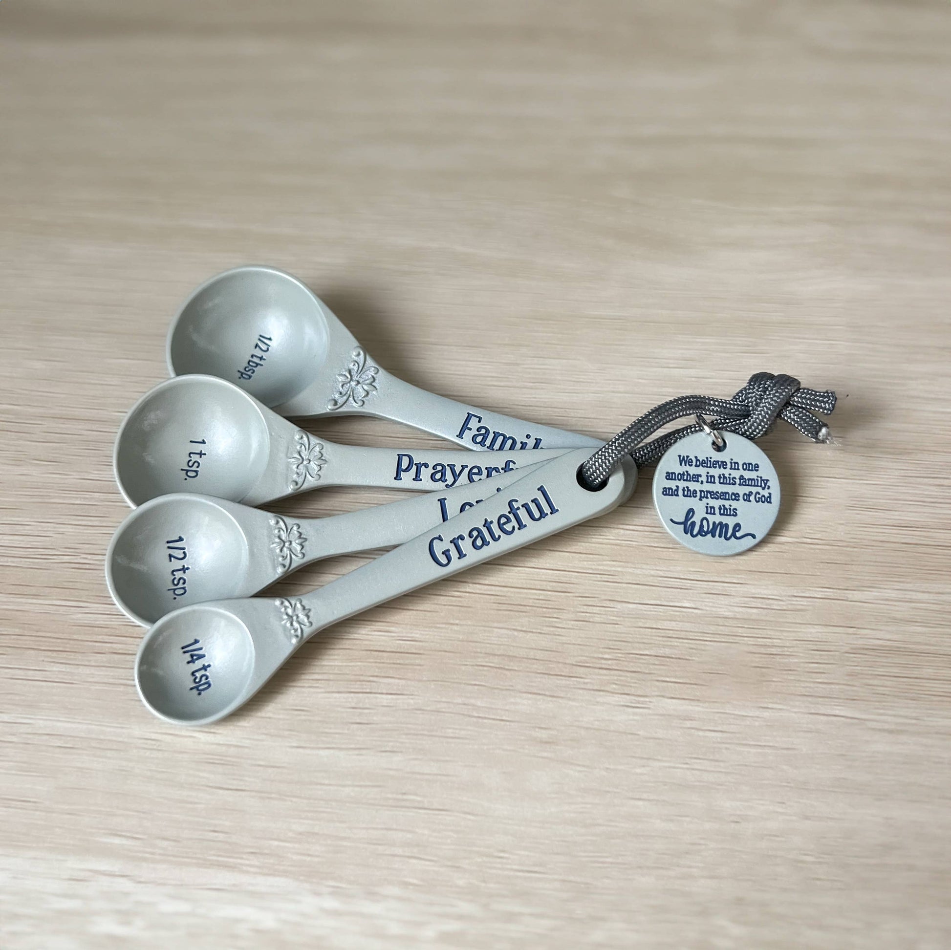 Set of five silver measuring spoons with engraved text on a wooden surface