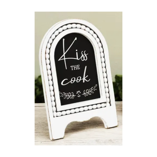 Decorative chalkboard sign with 'Kiss the Cook' text on a white stand.